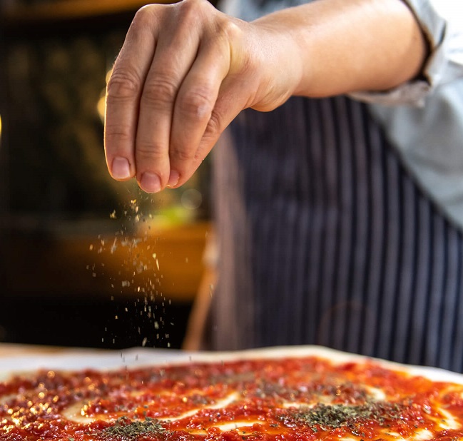 Sprinkling seasoning on a Tomato Pie.